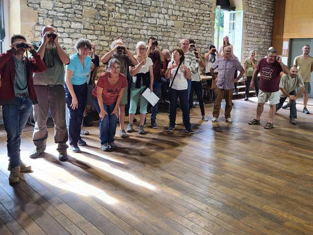 Groupe de personnes dans une salle aux murs en pierre, debout avec des jumelles ou prêtes à courir